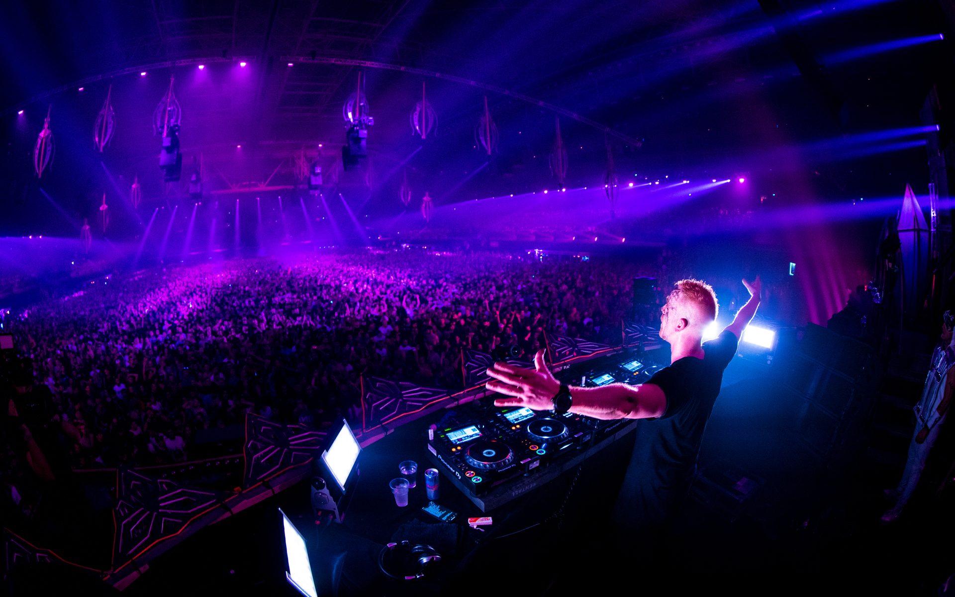 A DJ looking over the crowd and violet-lit stage at Qlimax.